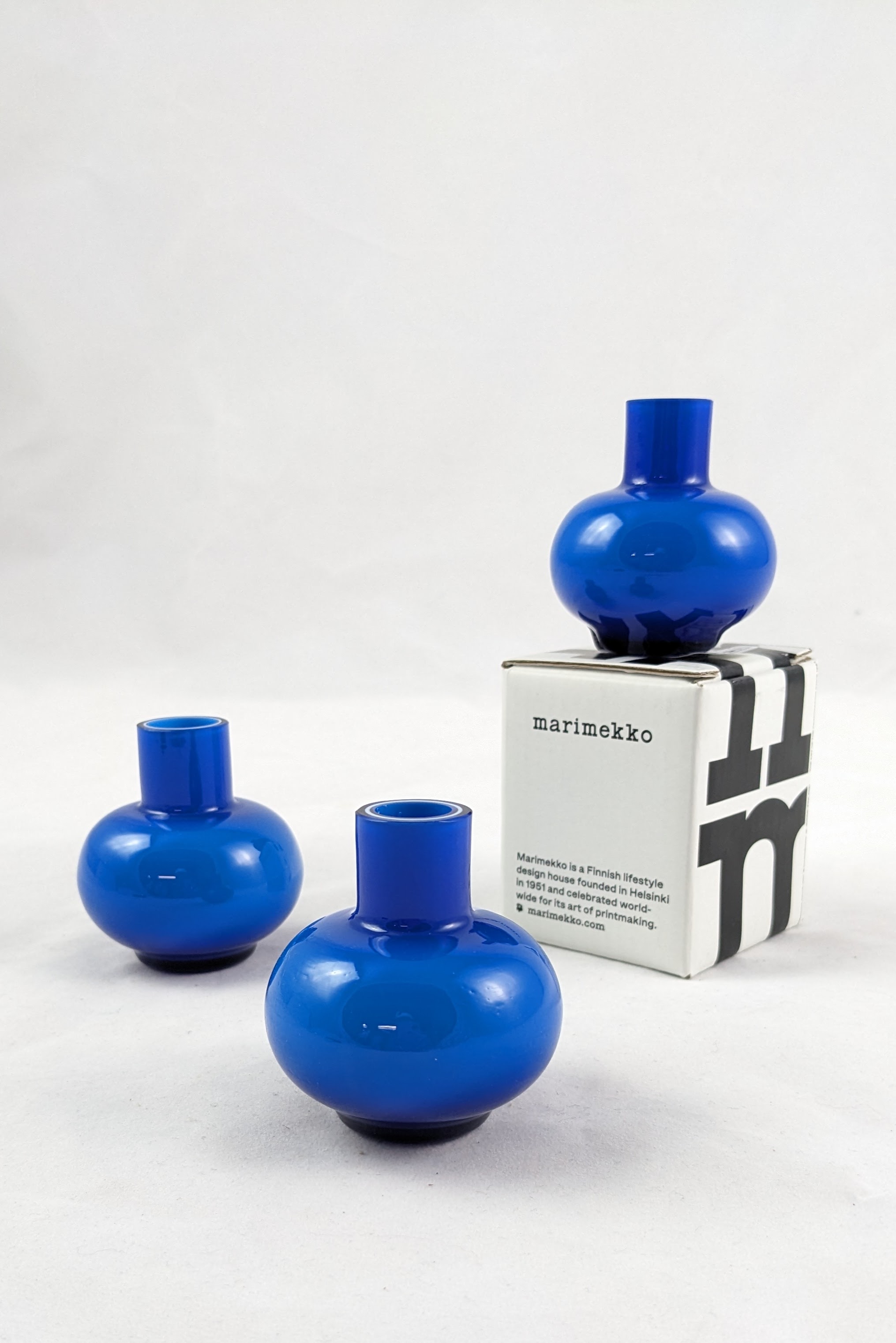 three royal blue glass vases, one is atop of of the white and black packaging