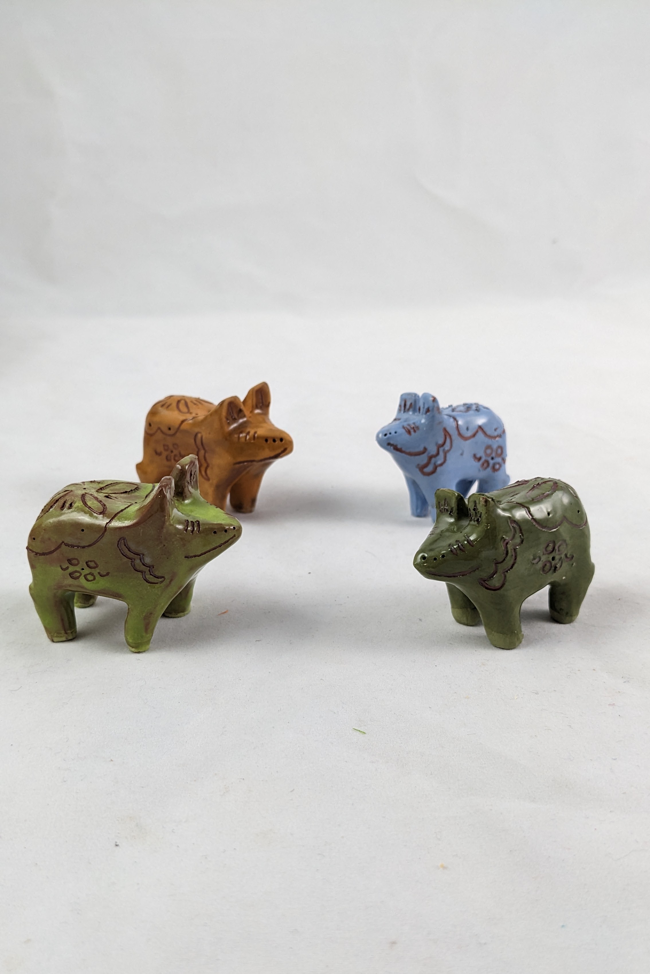 four dala pigs facing each other each in a different color: Light green, burnt orange, pastel blue, and khaki green. 